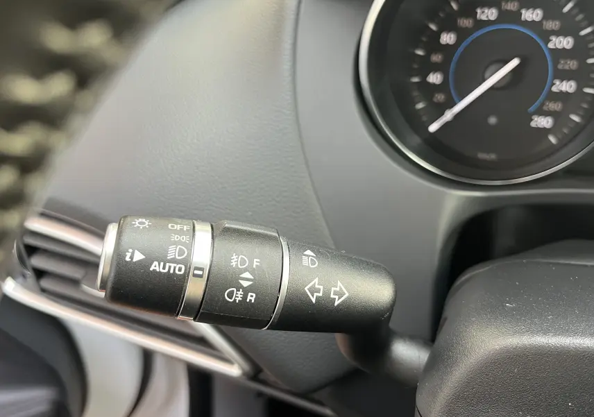 Gros plan sur la manette de clignotants et feux du tableau de bord d’un Jaguar F-PACE blanc, version 240D Prestige 2018.