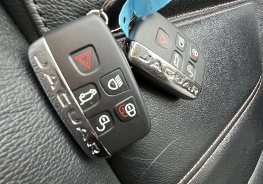 Gros plan sur deux clés Jaguar noires posées sur une sellerie cuir noir avec surpiqûres beiges.