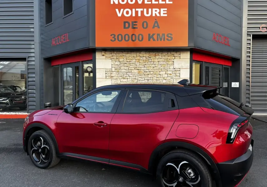 Vue latérale droite d'un Alfa Romeo Junior 1.2 Ibrida rouge avec toit noir et jantes noires au design distinctif.