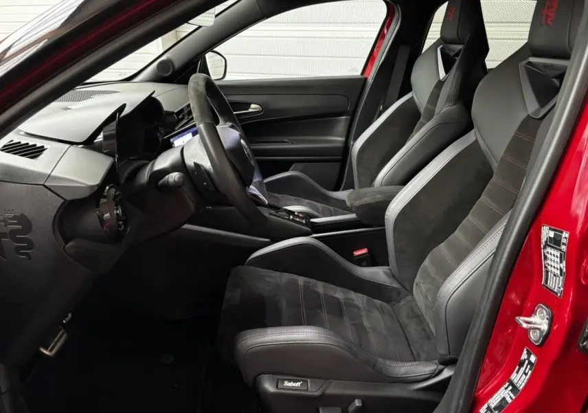 Vue intérieure côté conducteur de l'Alfa Romeo Junior rouge 2024 avec sièges sport Sabelt noirs et volant cuir multifonctions.