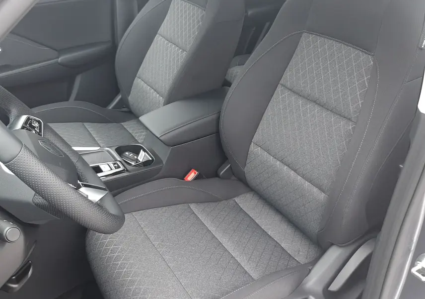 Vue intérieure côté conducteur du MG MOTOR ZS 1.5 HYBRID+ 197CH 2026, sièges tissu gris avec motifs losanges.