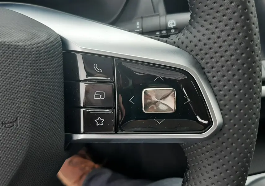 Gros plan sur les commandes à gauche du volant perforé du MG MOTOR ZS 1.5 HYBRID+ 197CH Camden Grey, année 2026.