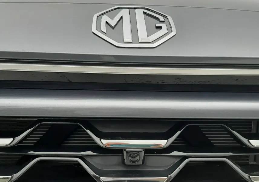 Gros plan sur la calandre avant grise Camden du MG ZS 1.5 HYBRID+ 197CH avec logo MG et caméra frontale intégrée.