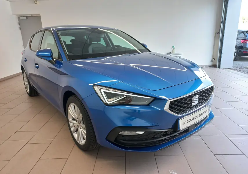 SEAT Leon 1.5 eTSI 115 DSG7 Copa bleu saphir en 3/4 avant droit, intérieur showroom lumineux.