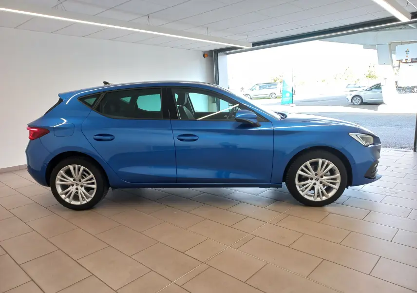 Profil côté gauche d'une SEAT LEON 1.5 eTSI 115 DSG7 COPA en bleu saphir, avec vitres arrière surteintées en intérieur showroom.