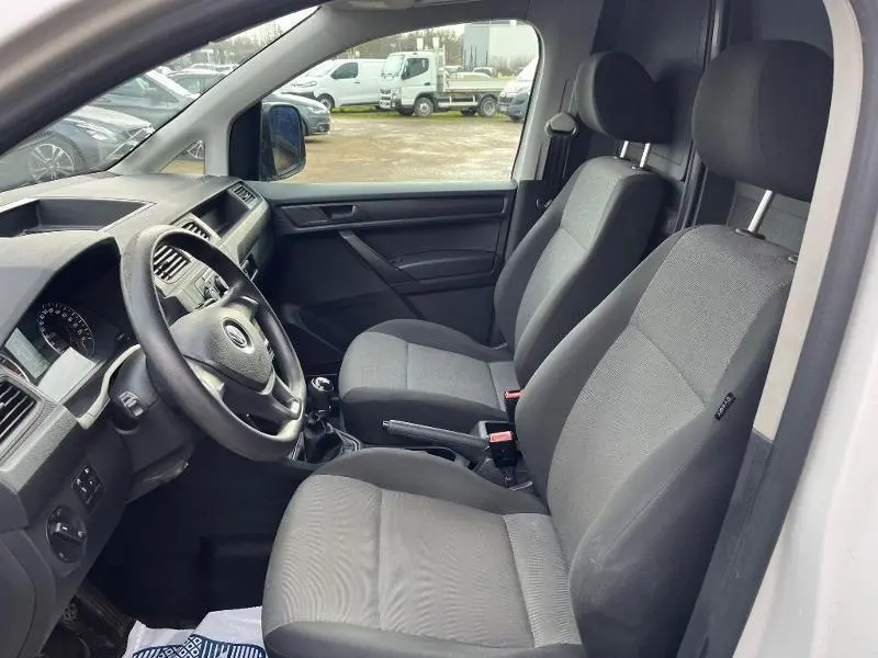 Intérieur du Volkswagen Caddy Van blanc, vue côté gauche montrant les sièges avant en tissu gris et le tableau de bord.