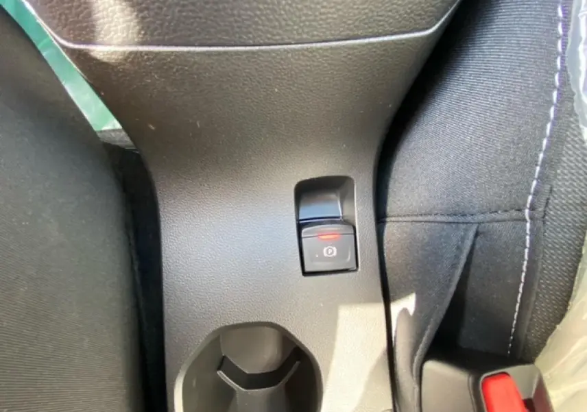 Gros plan sur le frein à main électronique et porte-gobelet entre les sièges avant d'une Dacia Logan gris 2022.