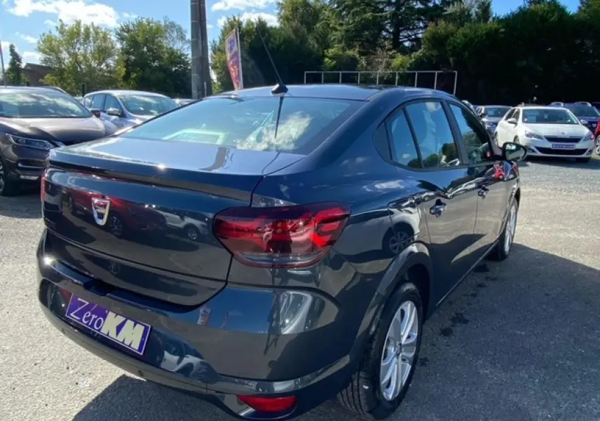 Vue 3/4 arrière droite d'une Dacia Logan gris métallisé 2022 avec radar de recul et caméra de stationnement visible.