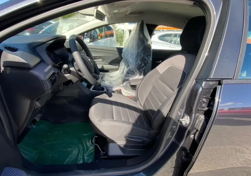 Intérieur côté conducteur de la Dacia Logan gris 2022, sièges en tissu gris et volant multifonction visible.