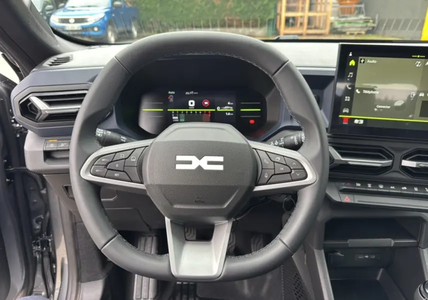 Vue intérieure centrée sur le volant du Dacia Duster 2025 gris schiste, avec tableau de bord numérique et écran tactile.