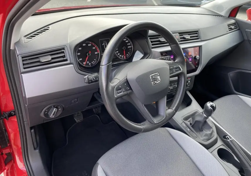 Vue intérieure côté conducteur d'une SEAT IBIZA rouge pur 2021, volant cuir multifonctions et boîte manuelle visibles.