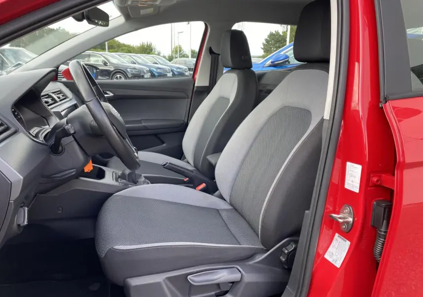 Vue intérieure côté conducteur de la SEAT IBIZA rouge pur 2021, avec sièges tissu gris et volant cuir multifonctions.