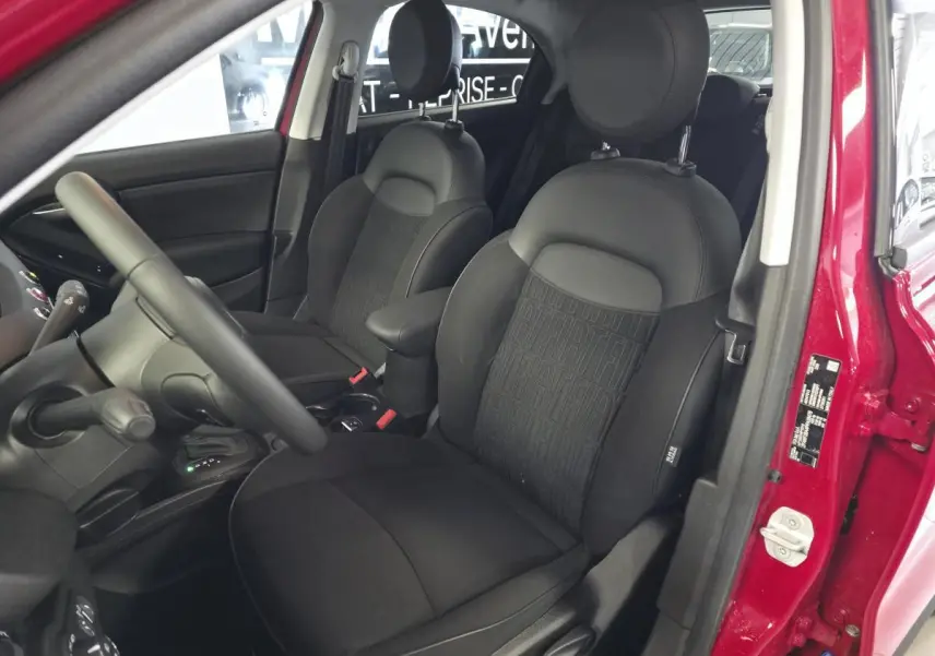 Vue intérieure côté conducteur du Fiat 500X rouge 2024, sièges tissu noir avec monogramme FIAT et accoudoir central.