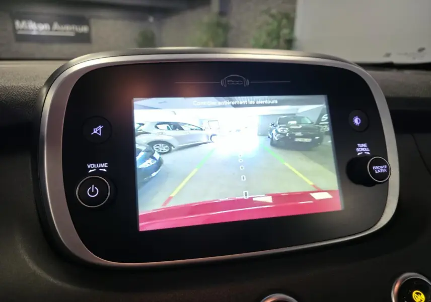 Écran multimédia de la Fiat 500X rouge montrant la caméra de recul avec vue arrière en parking intérieur.