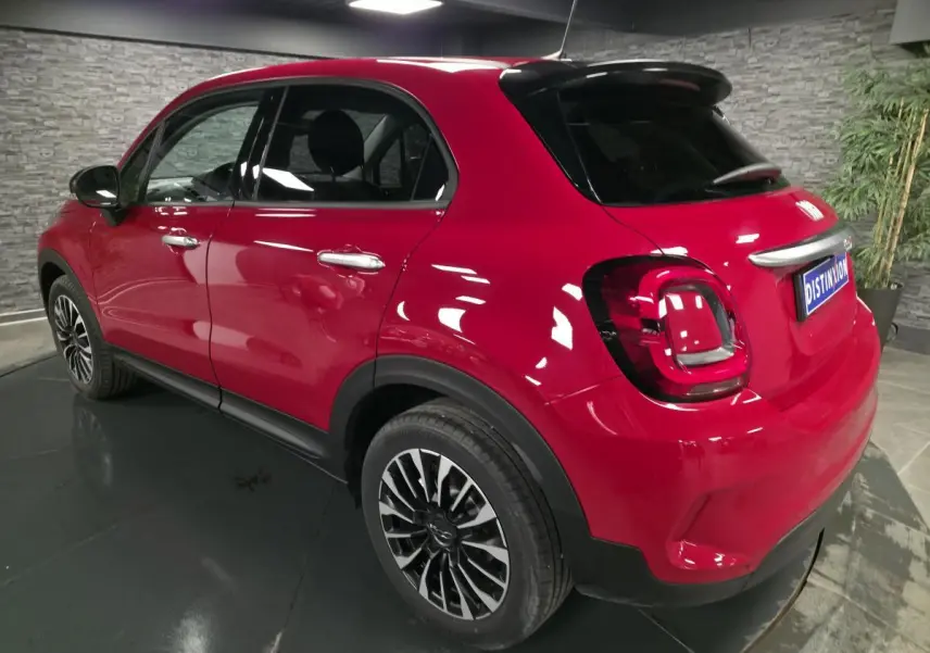 Vue 3/4 arrière droite d'une Fiat 500X rouge Passione avec jantes alliage 17 pouces et vitres surteintées.