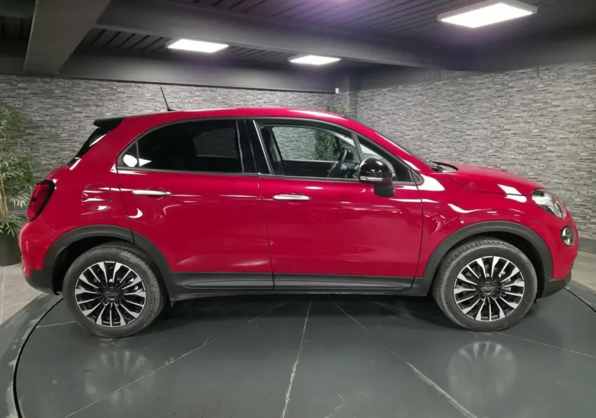 Vue latérale droite d'un Fiat 500X rouge avec jantes alliage noires et vitres surteintées dans un showroom.