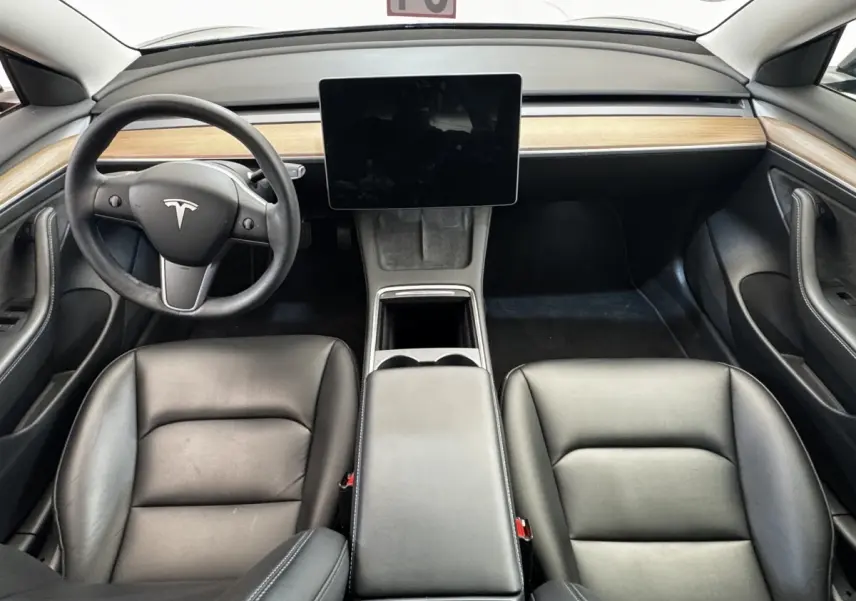 Vue intérieure frontale du tableau de bord et des sièges noirs en cuir d'une Tesla Model 3 2023 avec écran tactile central.