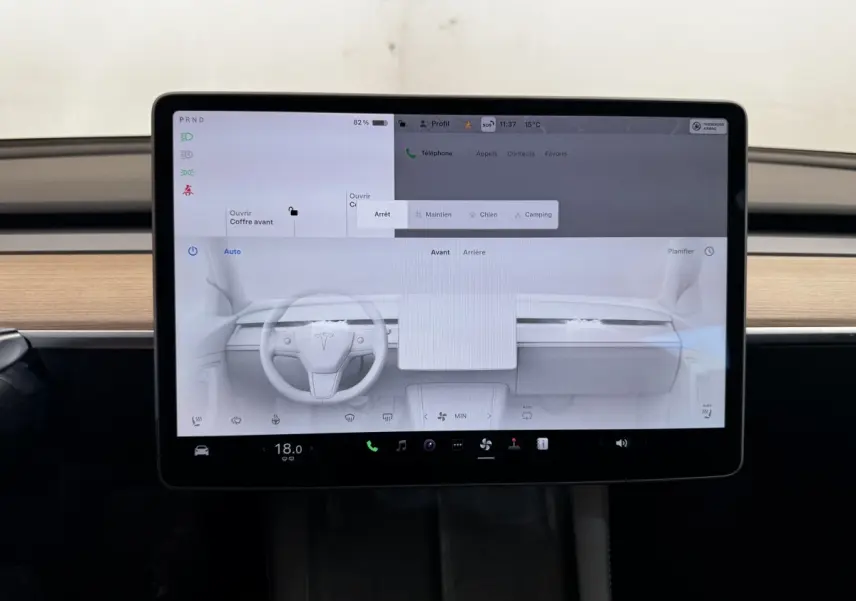 Écran tactile central affichant l’interface de la Tesla Model 3 2023, intérieur bois clair visible en arrière-plan.
