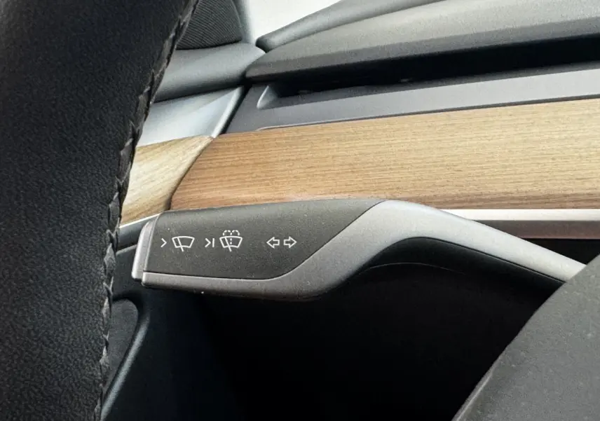 Gros plan sur la commande des essuie-glaces et clignotants dans l’habitacle bois et noir d’une Tesla Model 3 2023.