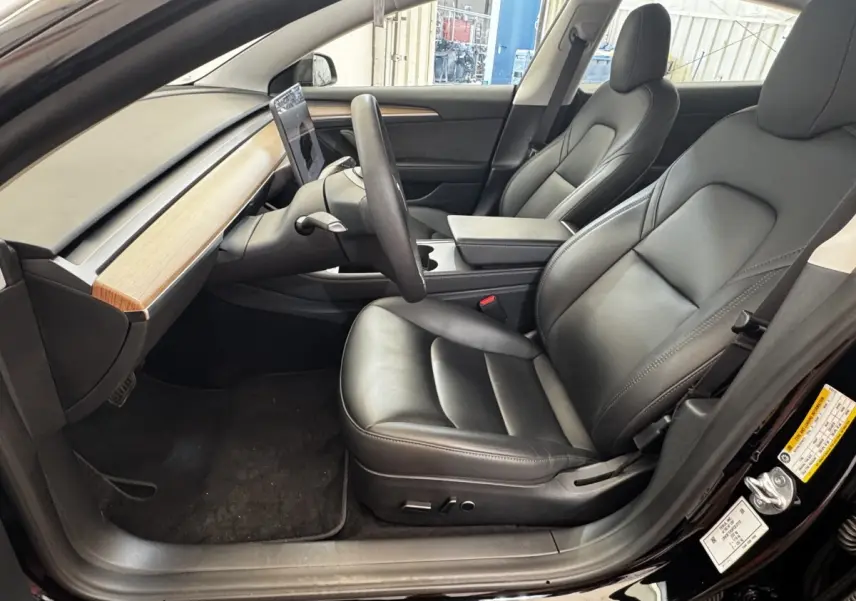 Intérieur côté conducteur de la Tesla Model 3 noire 2023, sièges cuir noir et tableau de bord bois clair.