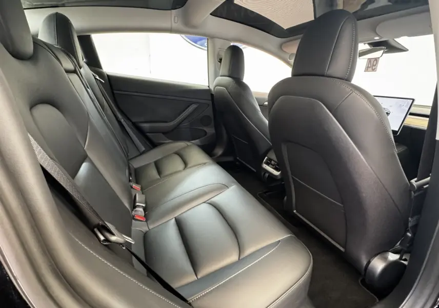 Intérieur arrière de la Tesla Model 3 noire 2023, vue côté gauche montrant les sièges en cuir et le toit panoramique.