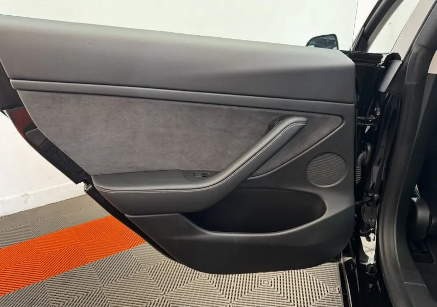 Vue côté intérieur de la porte arrière gauche noire d'une Tesla Model 3 2023 avec garniture tissu et cuir.