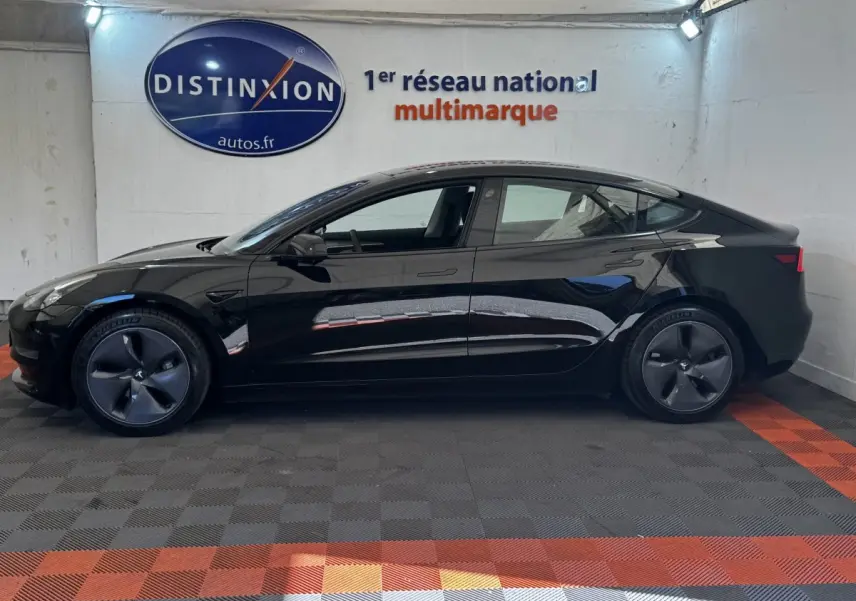 Profil côté gauche d'une Tesla Model 3 noire 2023 Grande Autonomie, roues aérodynamiques et intérieur visible.