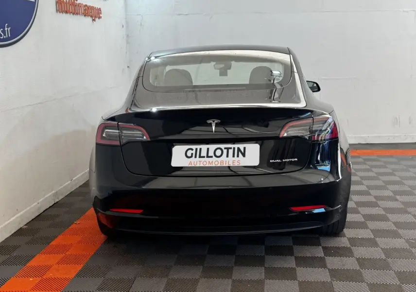 Vue arrière d'une Tesla Model 3 noire 2023 Grande Autonomie, avec feux LED et logo central lumineux.