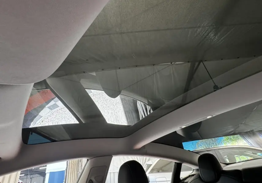 Vue intérieure du toit panoramique en verre d'une Tesla Model 3 noire 2023, avec sièges avant en cuir noir visibles.