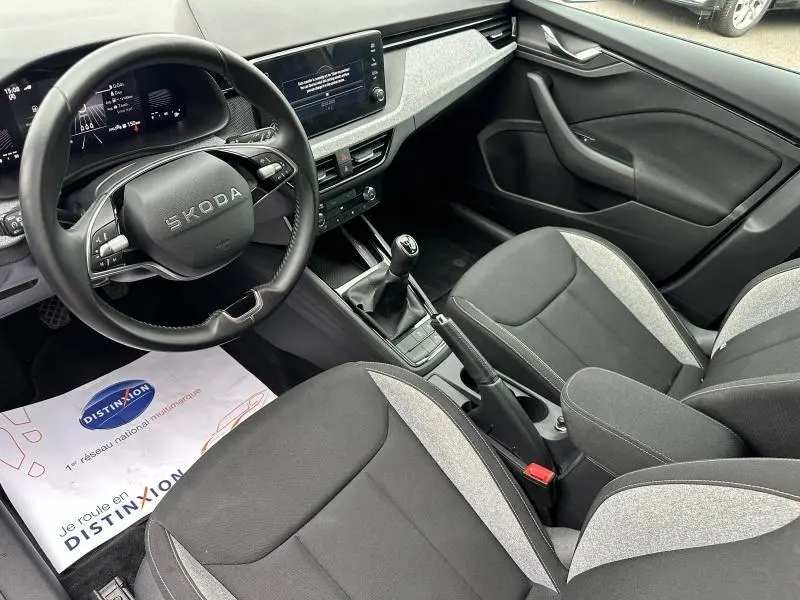 Vue intérieure côté conducteur de la Skoda Scala blanche, avec volant cuir, levier de vitesse manuel et sièges bi-ton gris et noir.