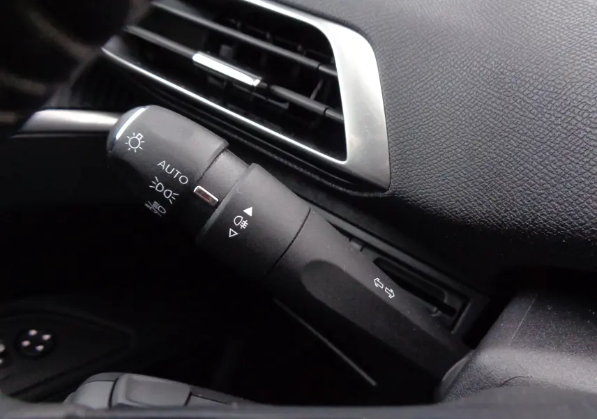 Gros plan sur la commande des phares et clignotants du Peugeot 3008 gris, avec tableau de bord texturé noir.