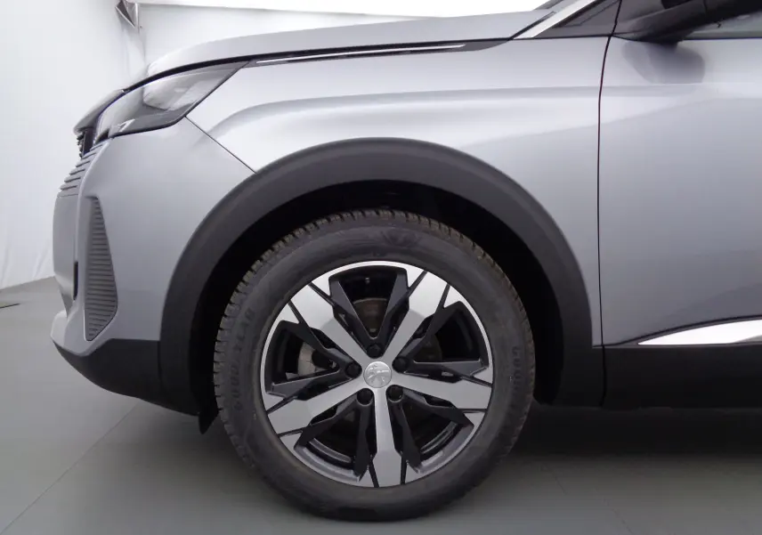 Gros plan sur la roue avant gauche et l'aile d'un Peugeot 3008 gris Artense métal avec jante bi-ton moderne.