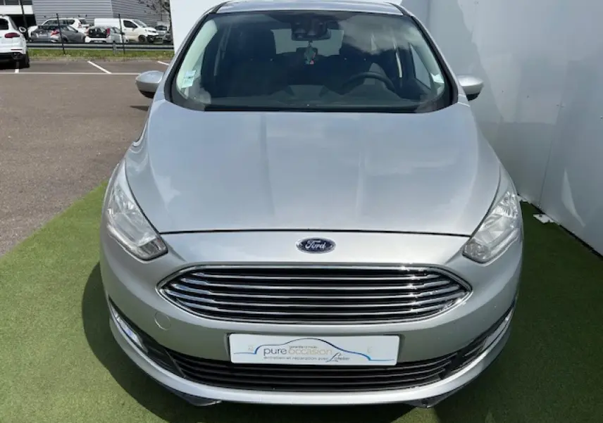 Vue avant d'une Ford C-MAX II gris clair métal avec calandre chromée et phares halogènes, stationnée sur sol vert.