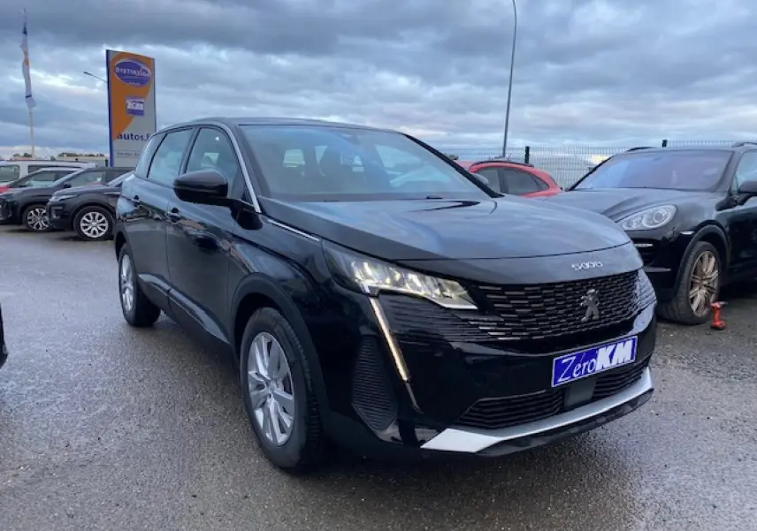 Peugeot 5008 noir vue 3/4 avant gauche sur parking, avec calandre distinctive et feux LED allumés.