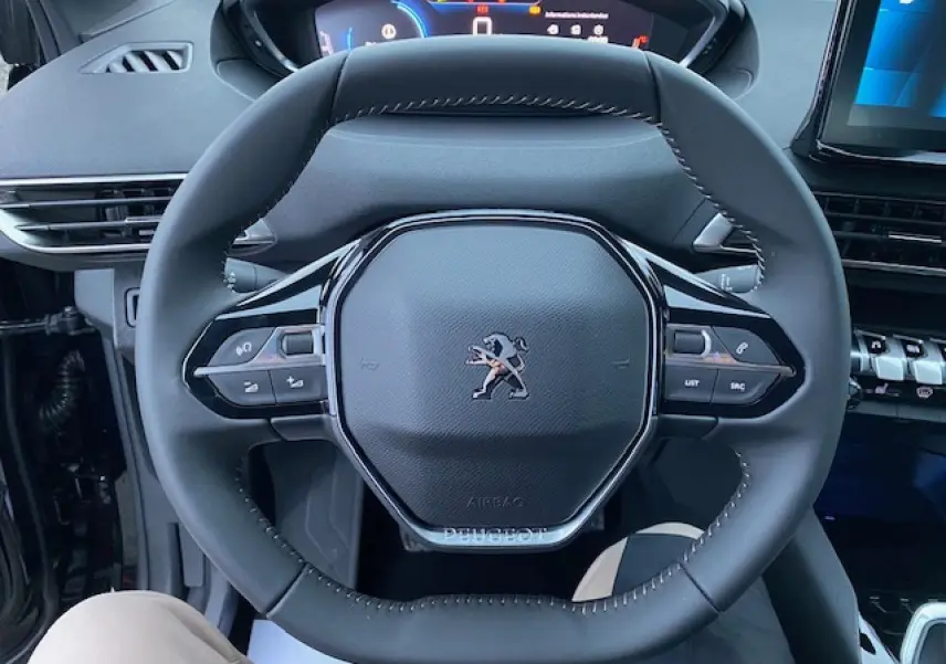 Vue rapprochée du volant cuir noir du Peugeot 5008 2023 avec commandes intégrées et tableau de bord digital.