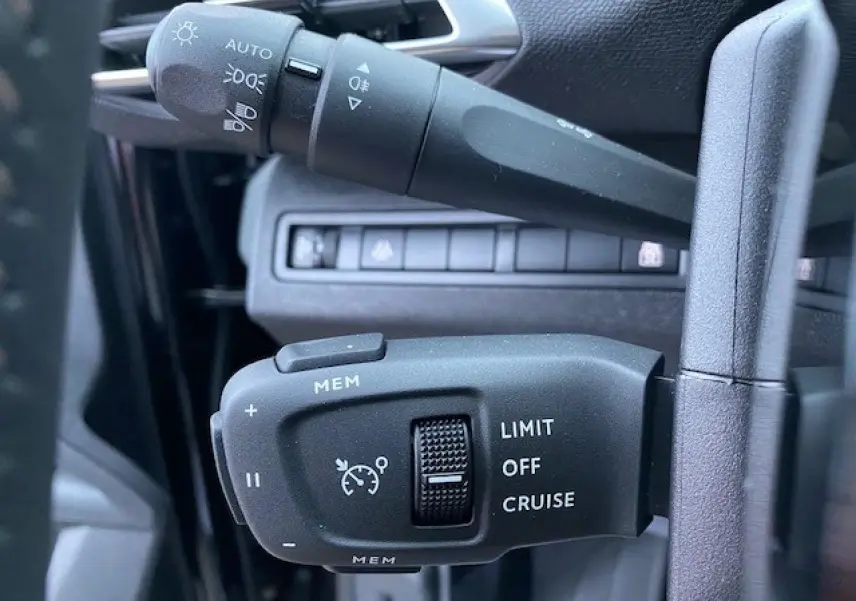 Gros plan sur les commandes de régulateur de vitesse et des feux sur la colonne de direction d'un Peugeot 5008 noir 2023.