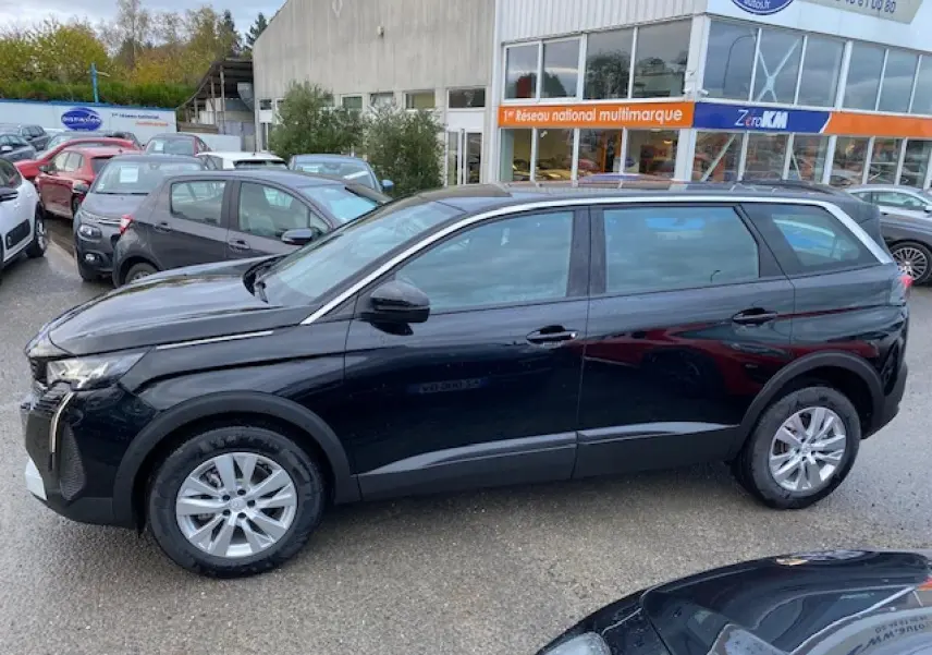 Peugeot 5008 noir vue de profil côté gauche, avec jantes alliage et carrosserie brillante sous un ciel nuageux.