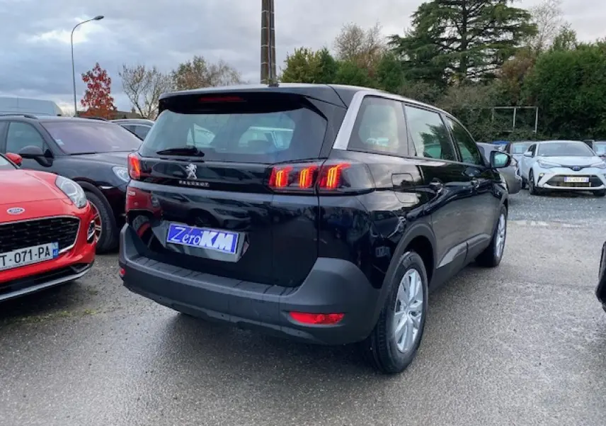 Peugeot 5008 noir vue 3/4 arrière droit, feux arrière LED allumés, jantes alliage 16 pouces, stationnée en extérieur.