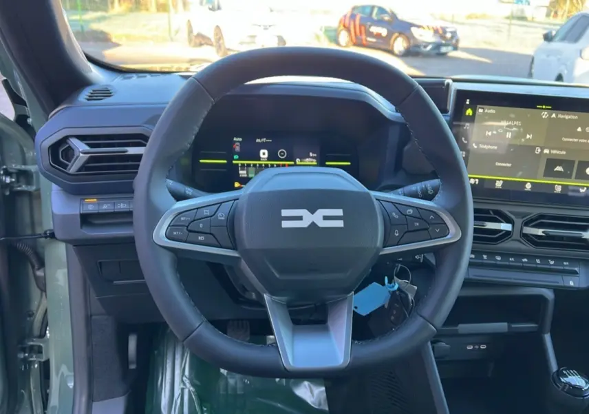 Vue intérieure centrée sur le volant du Dacia Duster 2025 kaki lichen, avec tableau de bord numérique et écran tactile.