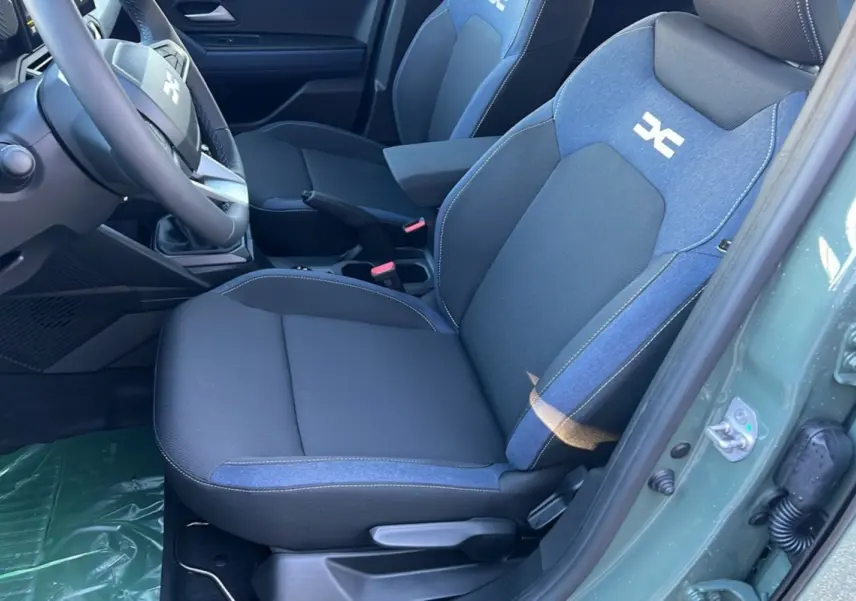 Intérieur du Dacia Duster 2025, siège avant droit en tissu noir et bleu avec logo blanc, portière kaki lichen ouverte.