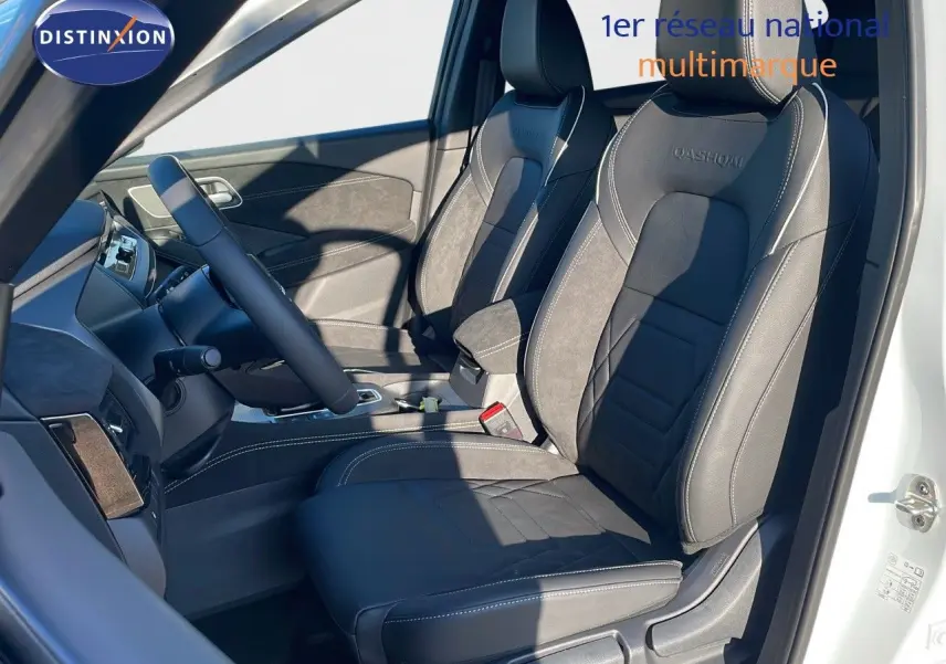 Intérieur du Nissan Qashqai 2025 en blanc nacré, vue côté gauche sur sièges en cuir noir avec logo Qashqai brodé.