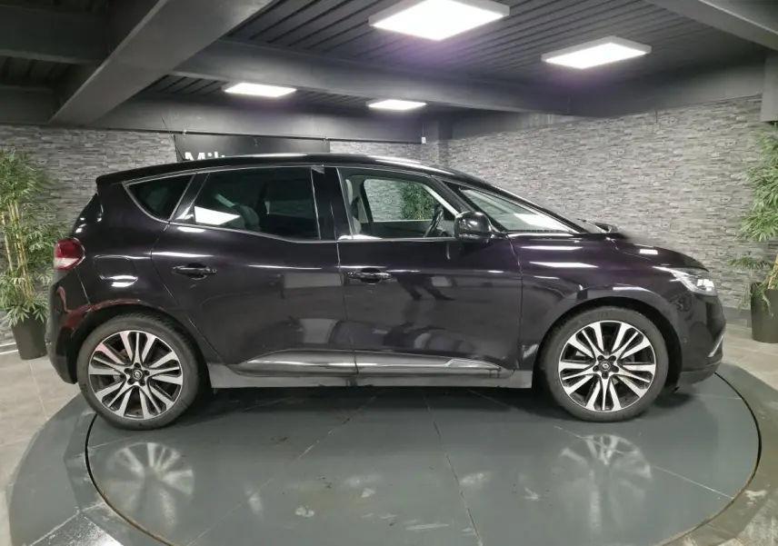 Profil droit d'un Renault Scénic noir Améthyste 2018 avec jantes alliage et toit panoramique fixe dans un showroom.