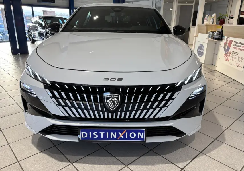 Vue de face d'une Peugeot 308 blanche Okenite avec calandre noire à motifs verticaux et logo lion lumineux.