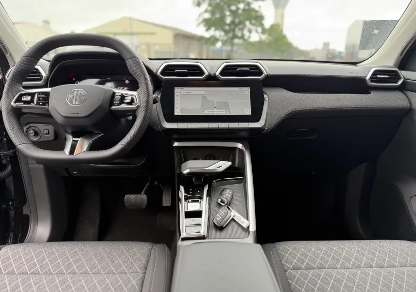 Vue intérieure frontale du tableau de bord et volant noir du MG ZS 1.5L Hybrid+ avec écran tactile et clés sur la console centrale.