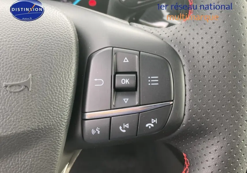 Vue rapprochée des commandes multifonctions côté gauche du volant perforé avec coutures rouges d'une Ford Focus gris 2025.