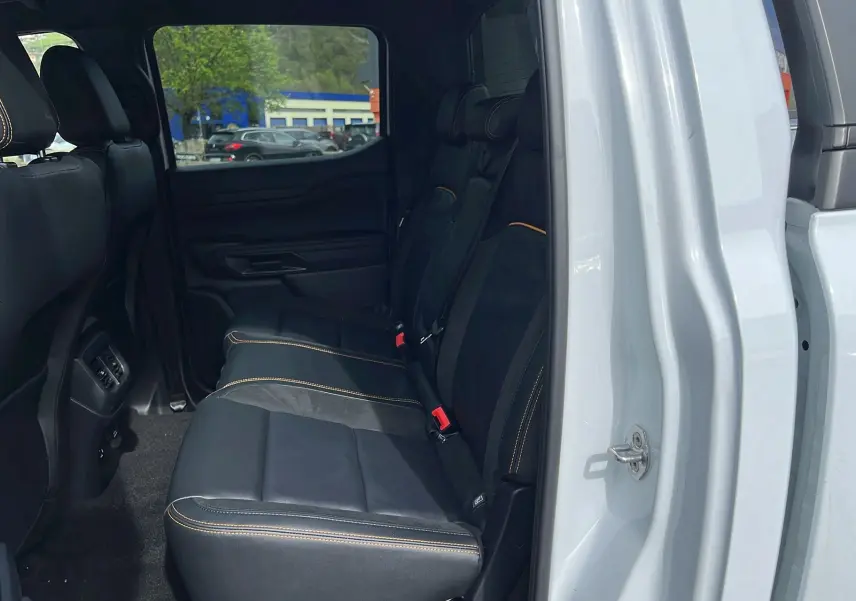 Vue latérale côté droit sur l’intérieur arrière noir avec surpiqûres orange du Ford Ranger blanc glacier double cabine.