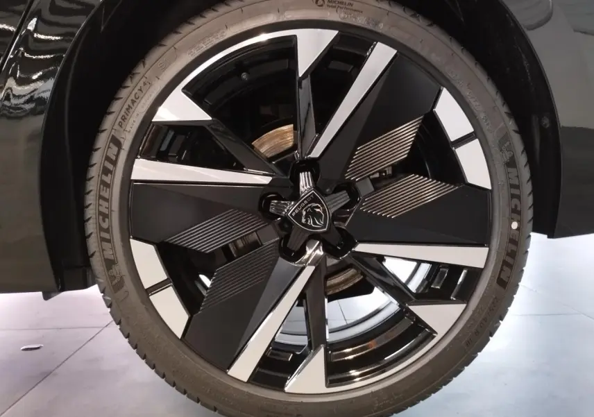 Gros plan sur la jante alliage bi-ton noir et argent avec logo Peugeot, montée sur une Peugeot 308 noire métallisée.