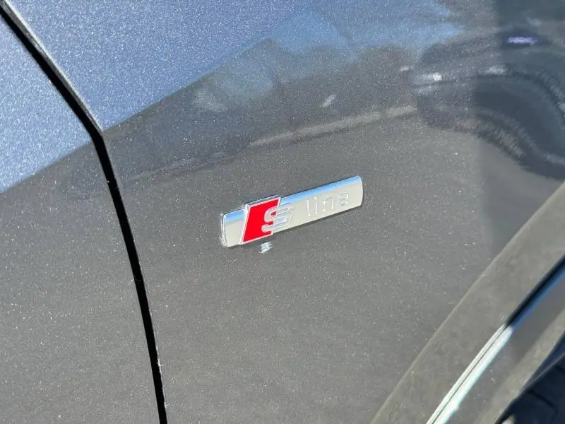 Détail de l'emblème S line sur la portière côté gauche d'un Audi Q2 35 TDI gris Daytona nacré 2025.