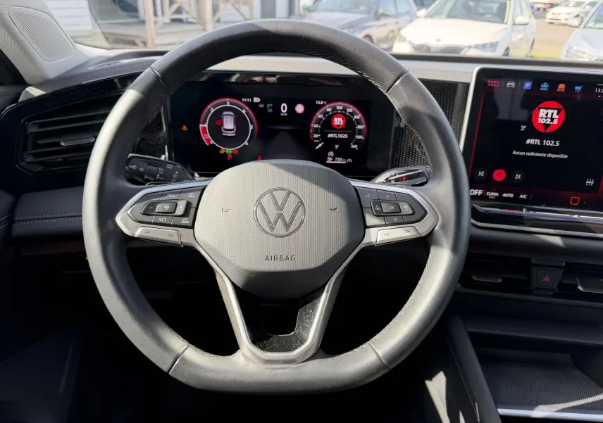 Vue intérieure centrée sur le volant cuir noir du Volkswagen Tiguan 2025 avec tableau de bord digital et écran tactile.