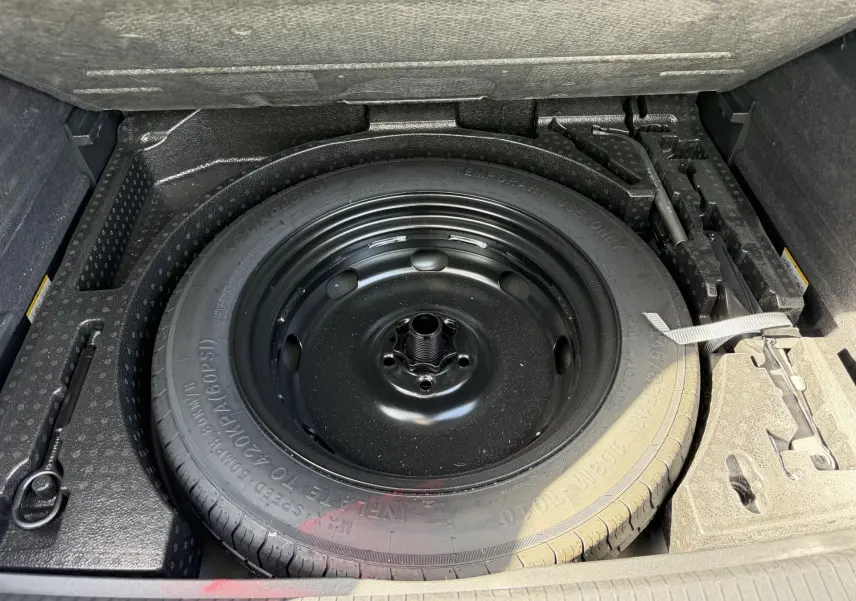 Vue plongeante sur la roue de secours compacte noire dans le coffre du Volkswagen Tiguan gris 2025.